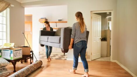 Two women carrying sofa out of a house